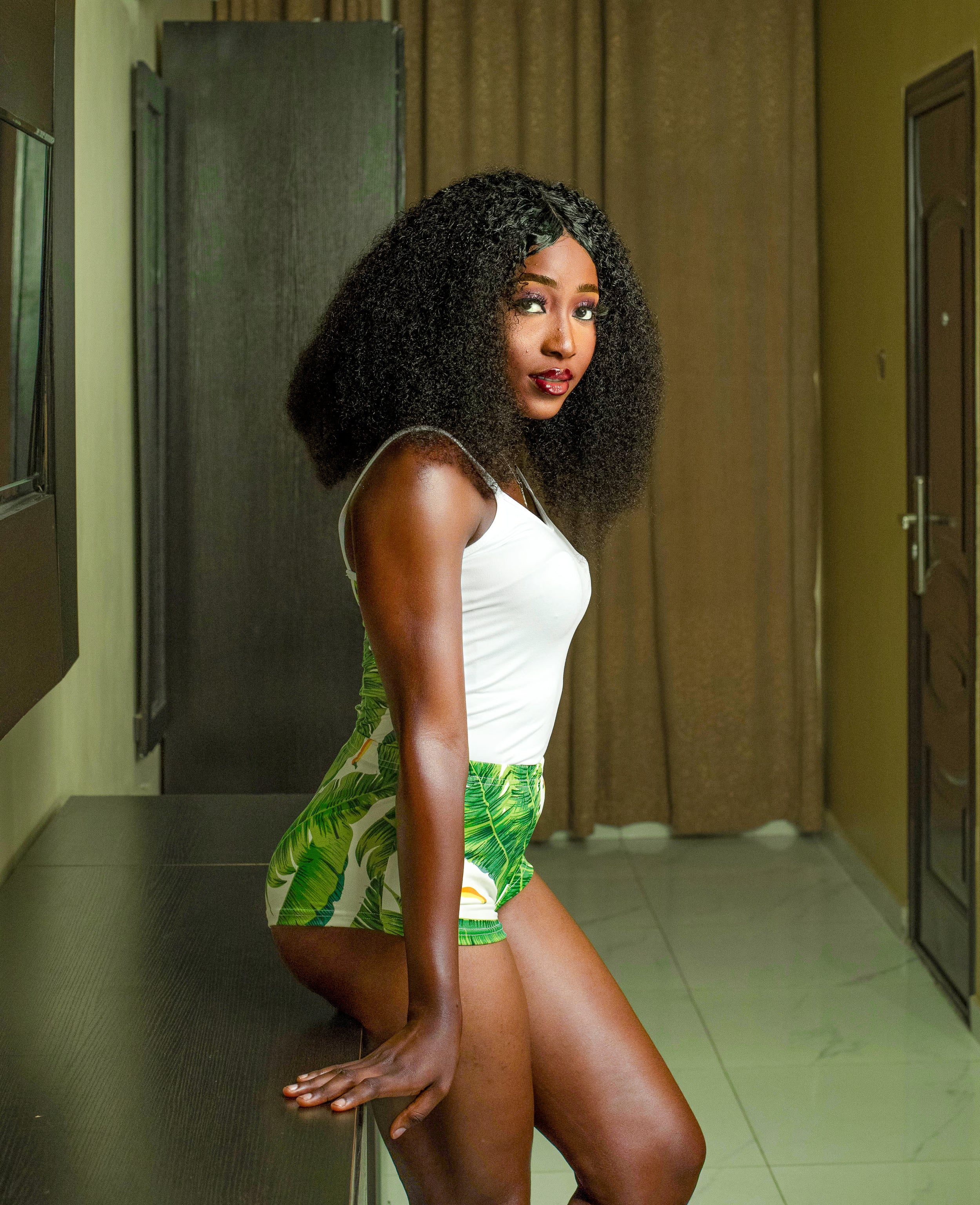 Woman in a white top and green leaf-patterned shorts posing in a room.