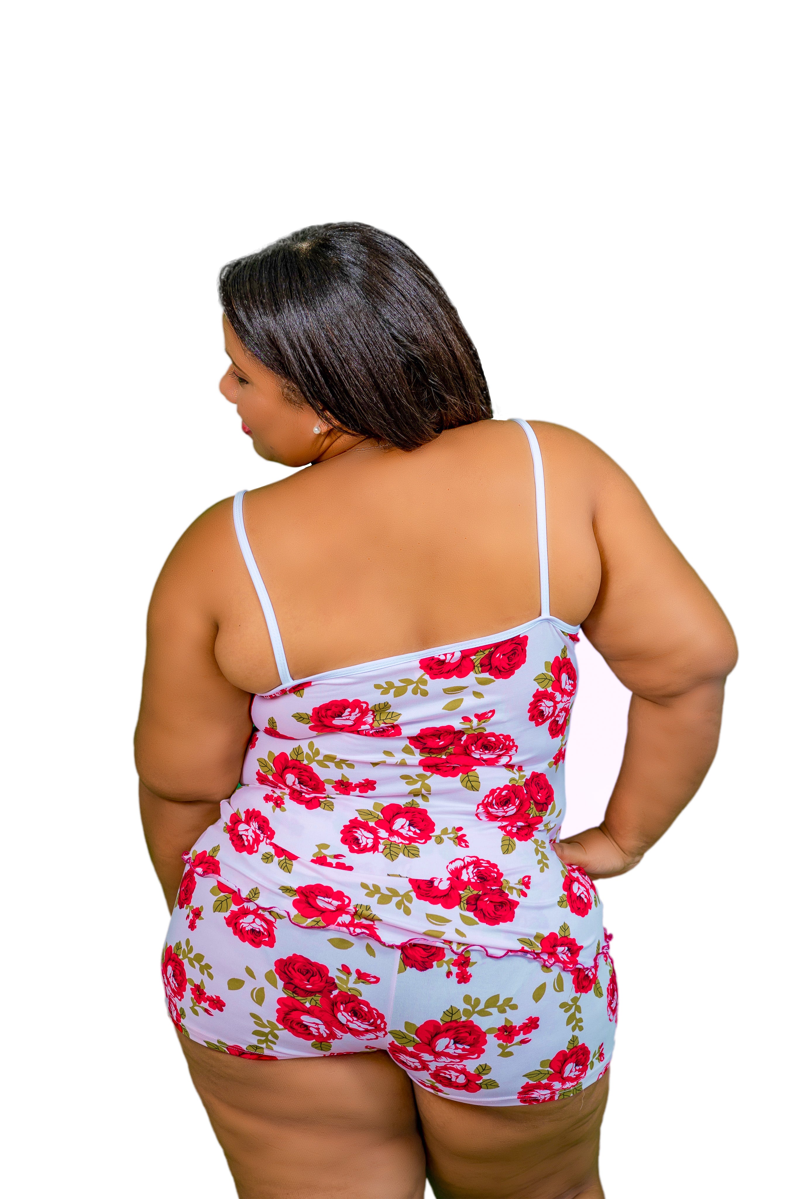 Woman with back turned  wearing a rose pajama short set with red flowers on a white background