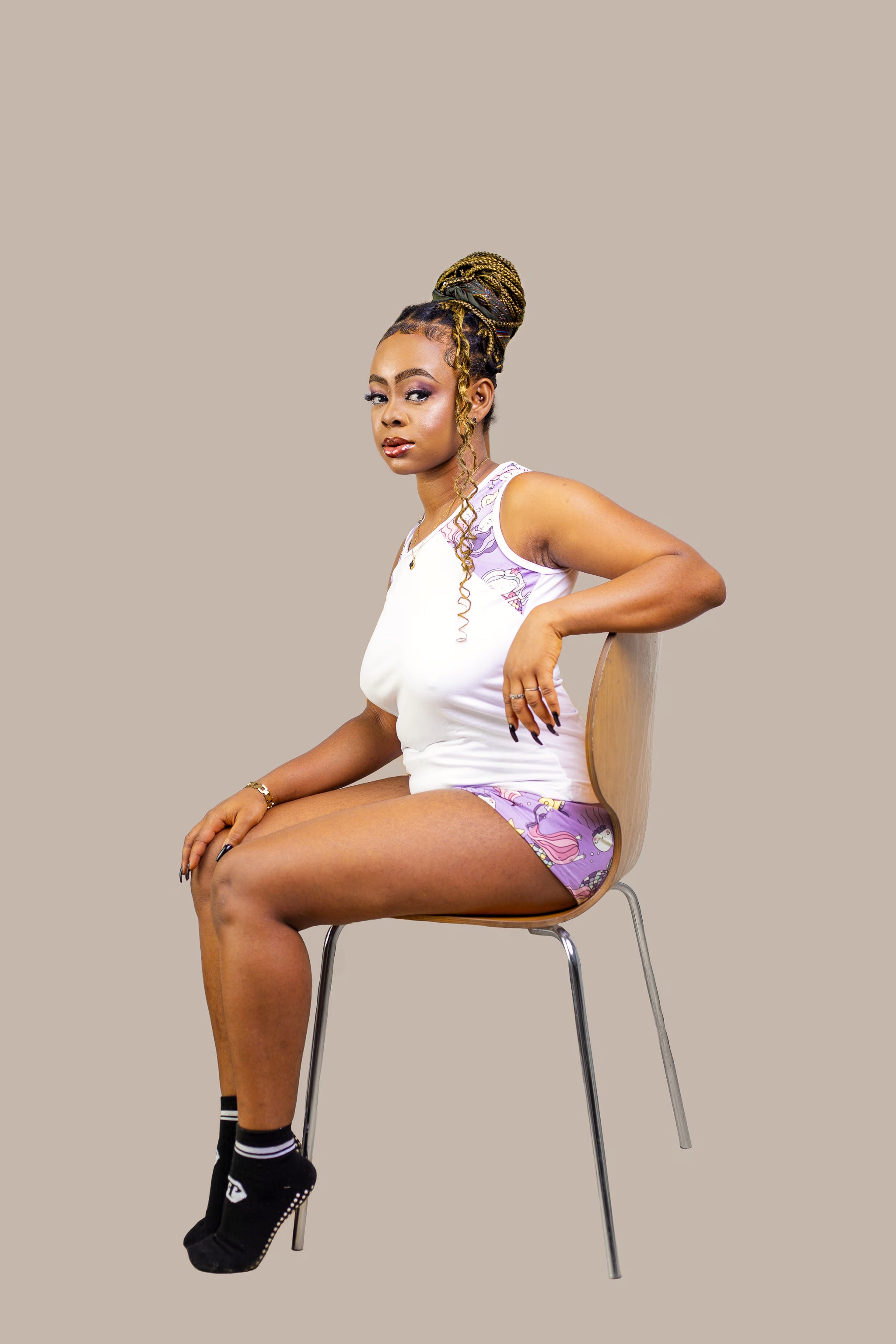 Woman sitting on a chair wearing a white top and patterned pajama shorts against a beige background