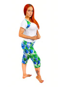 Woman wearing a white pajama t-shirt with colorful designs and blue and green patterned pajama capri shorts on a white background