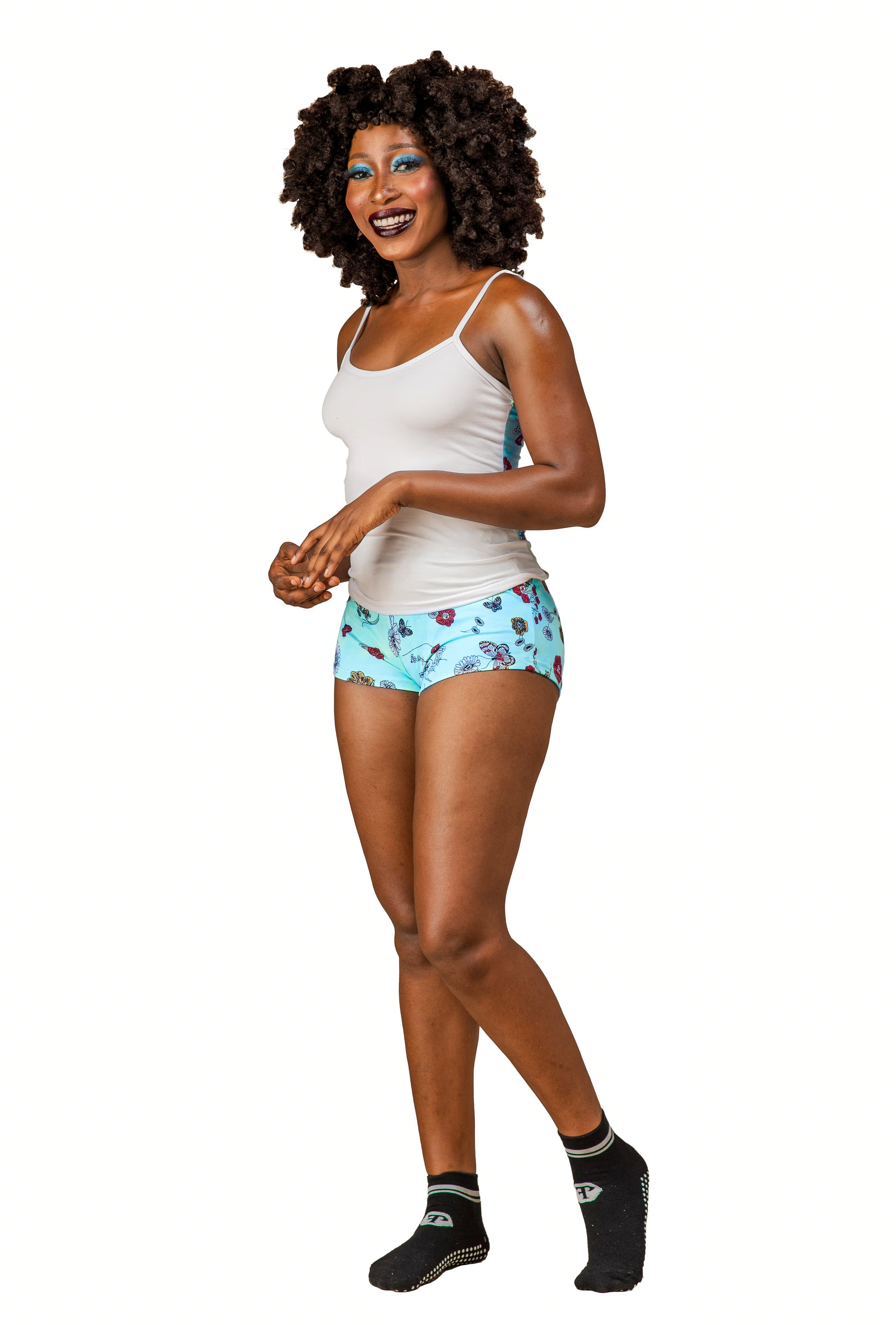 Woman wearing a white Cami top, multi-floral print shorts, and black socks on a white background
